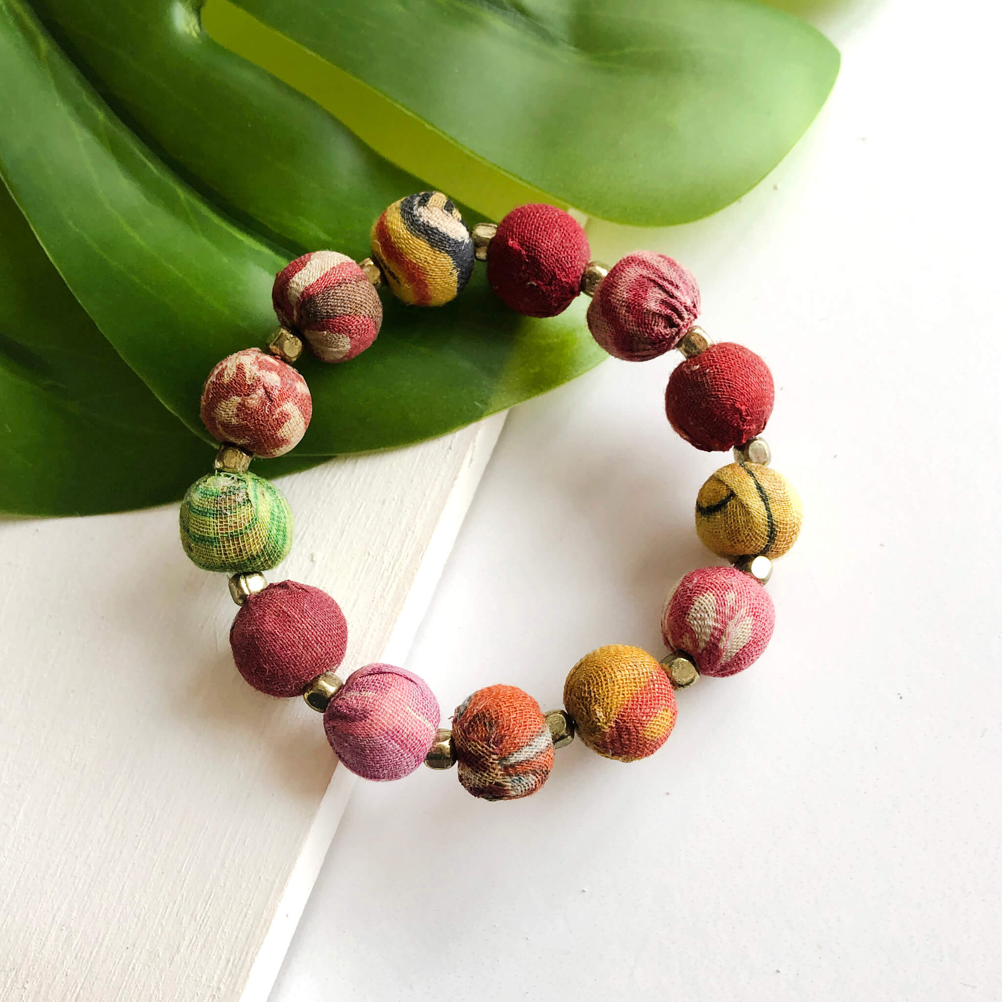 A multicolor beaded bracelet rests against a green leaf.