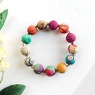 A multicolor beaded bracelet is against a white background with green leaves.