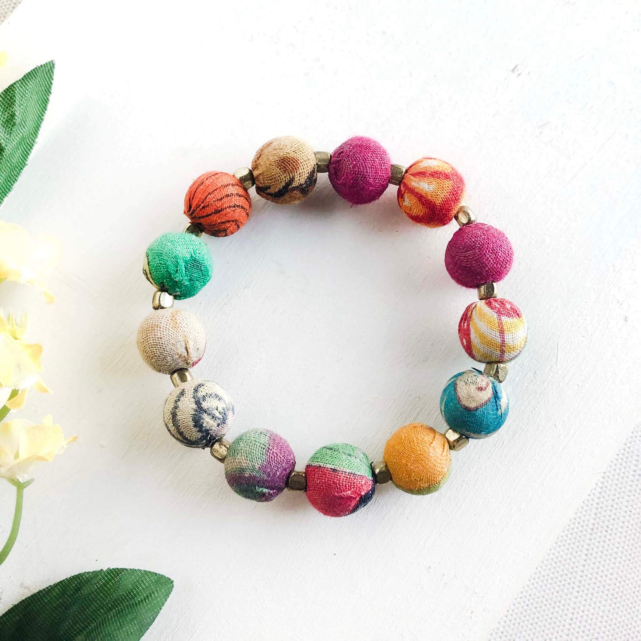 A multicolor beaded bracelet is against a white background with green leaves.