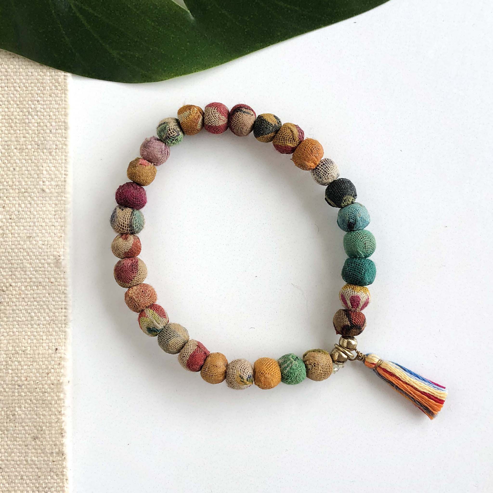 A multicolor beaded bracelet with a tassel against a white background with a green leaf in the background.