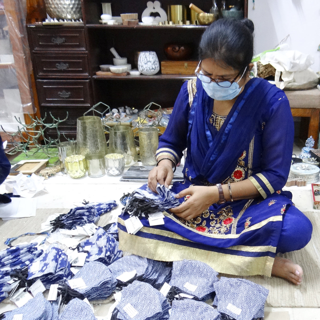 A woman artisan counts masks while sitting on the floor