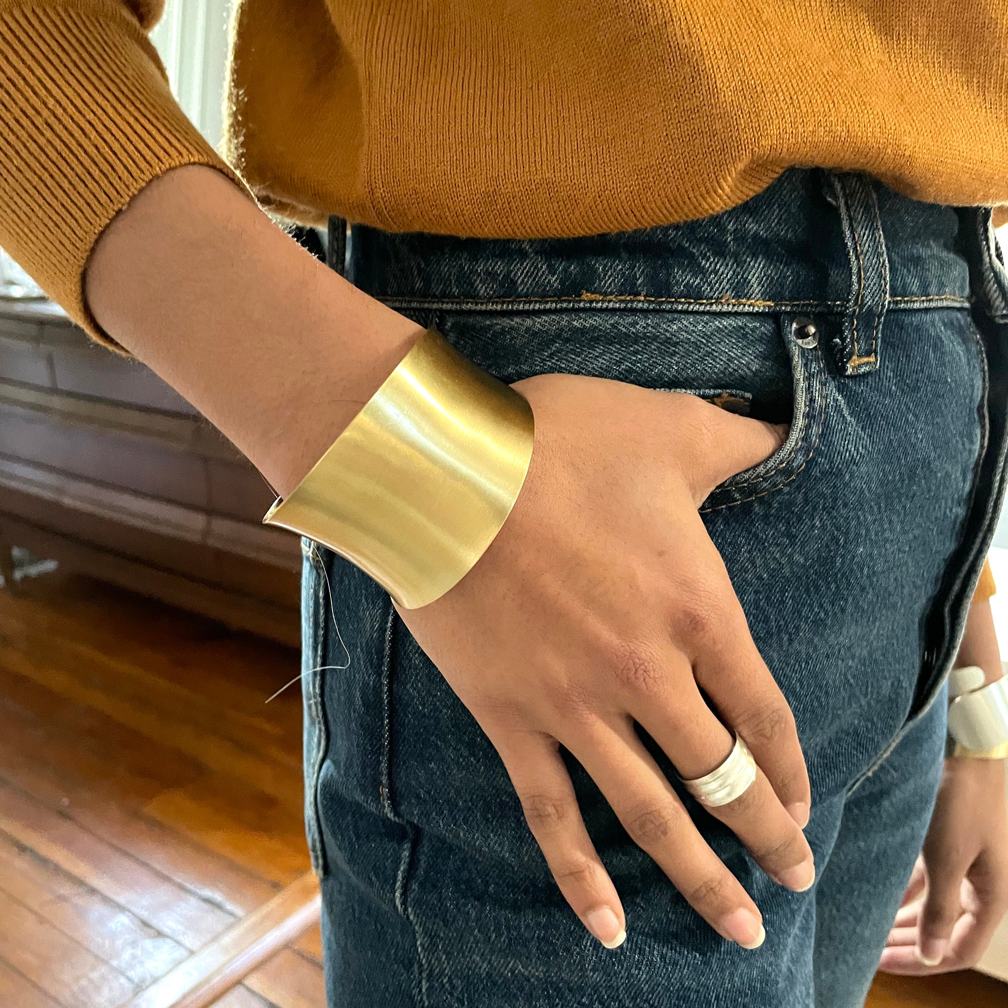 A woman's hand rests on her pant's pocket and her wrist is adorned with a gold cuff.