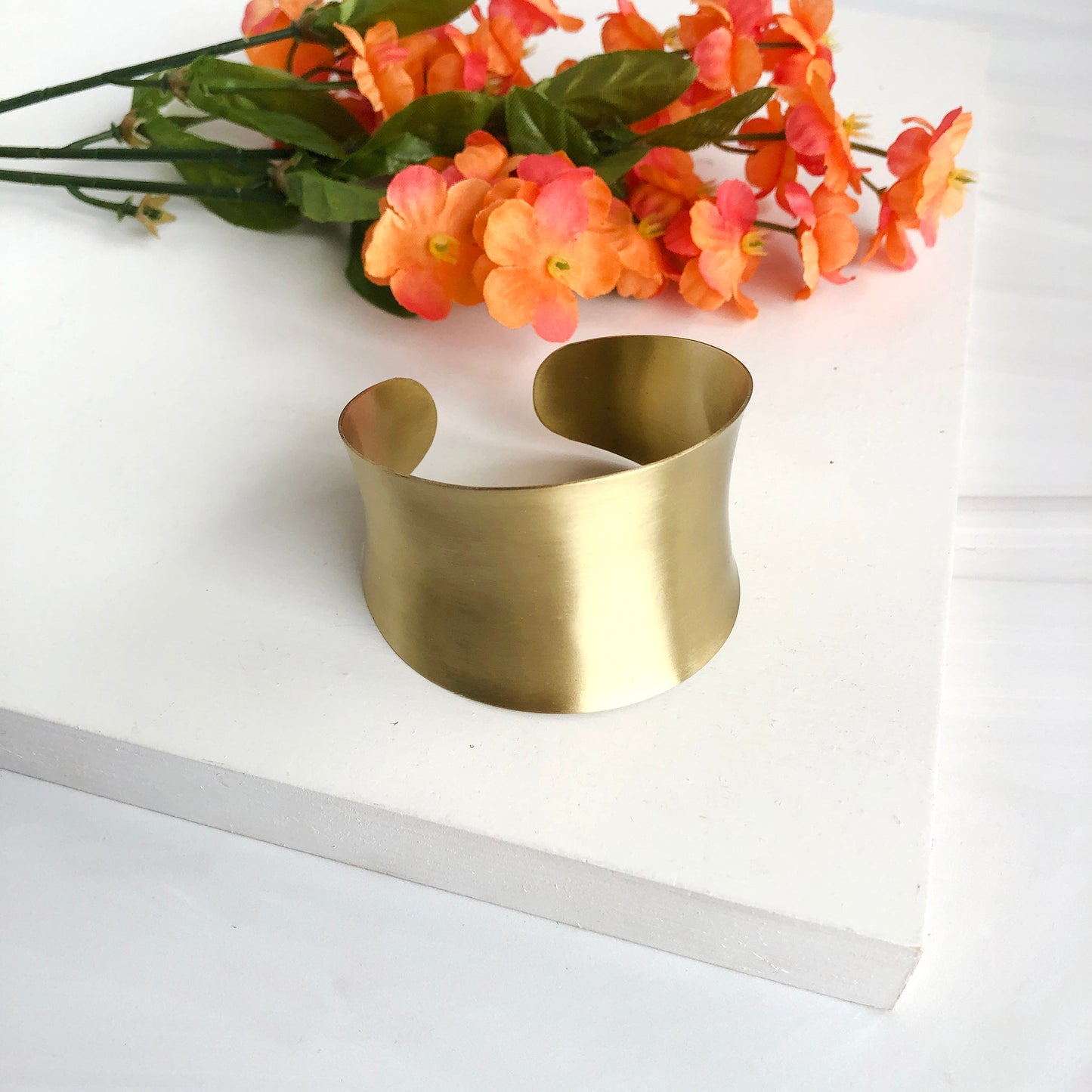 Load image into Gallery viewer, A tall gold cuff bracelet is seen with some orange flowers.
