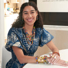 A woman smiles at us while adorned with colorful beaded jewelry and a large gold metallic cuff.