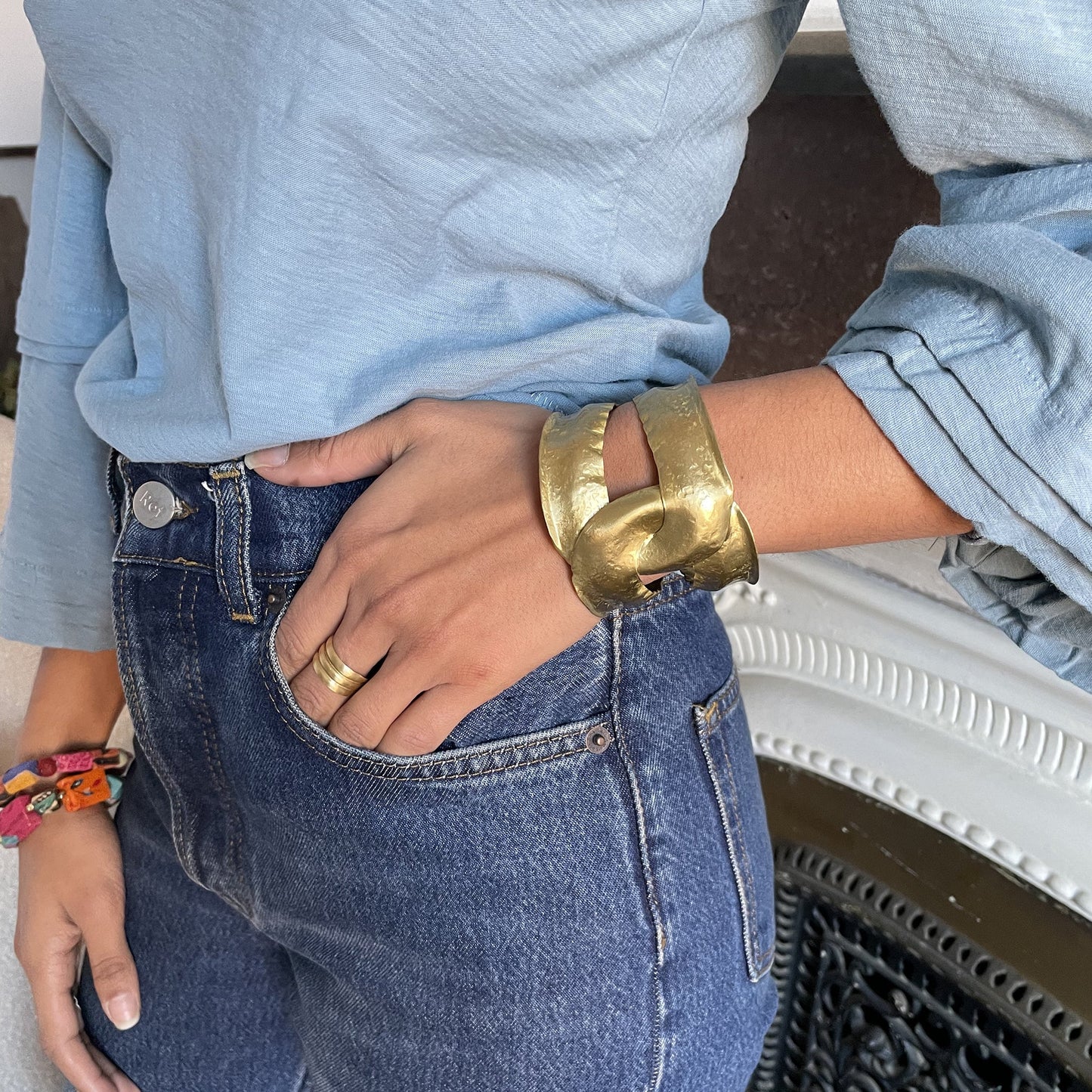 A woman's hand is slipped into her pocket and her wrist is adorned with a gold bracelet.