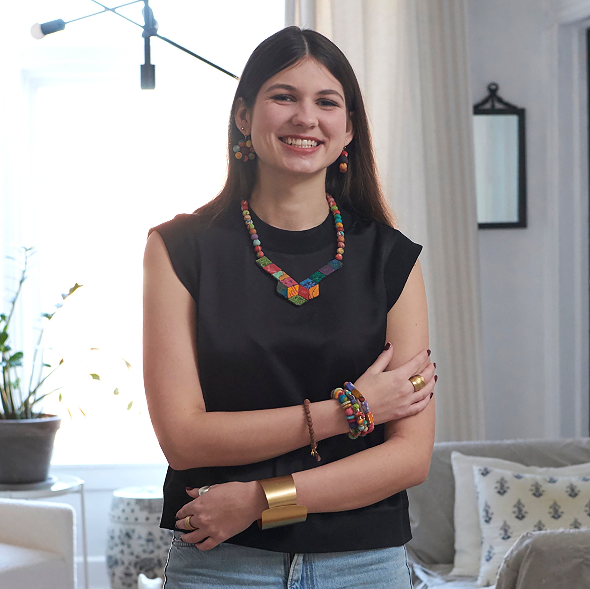 A woman smiles at us while modeling colorful beaded jewelry and a large gold cuff bracelet.