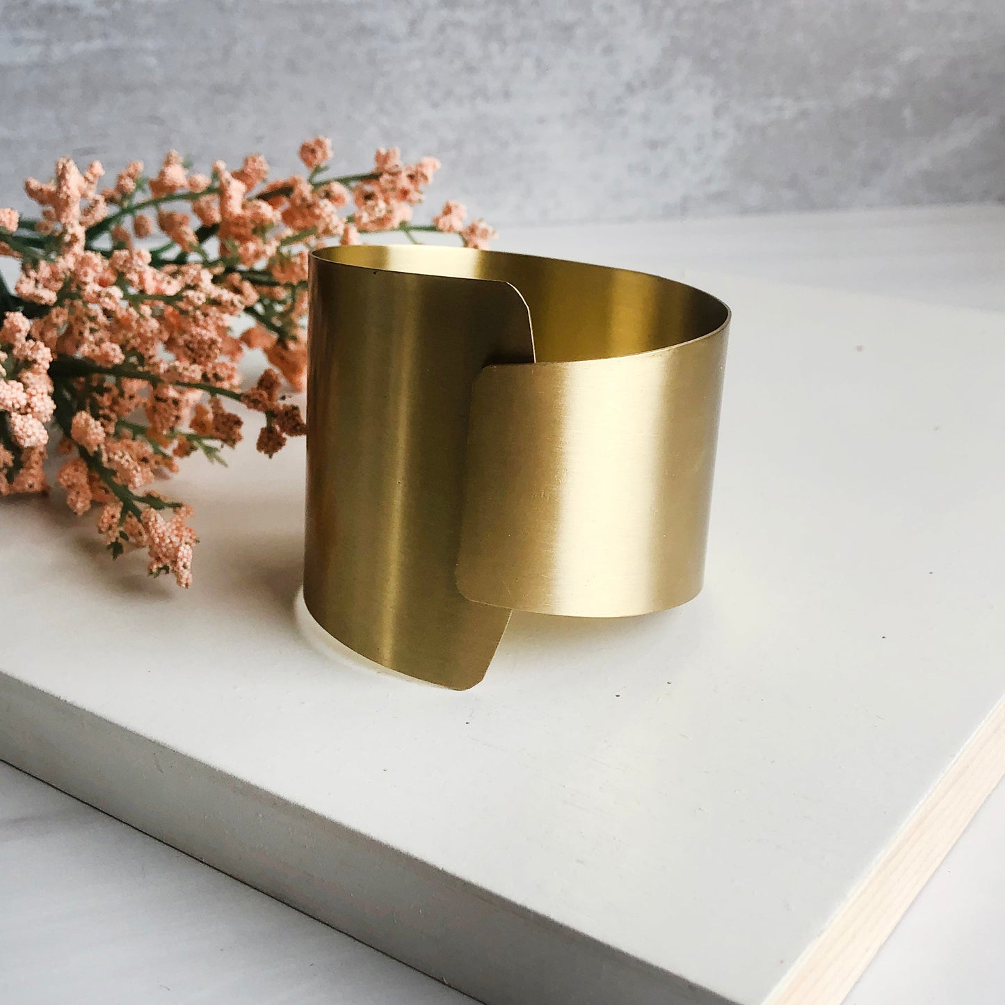 A thick band of metal wraps around and overlaps to form a large gold cuff bracelet.