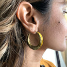 A woman's ear is shown wearing the gold Wavy Hoops.