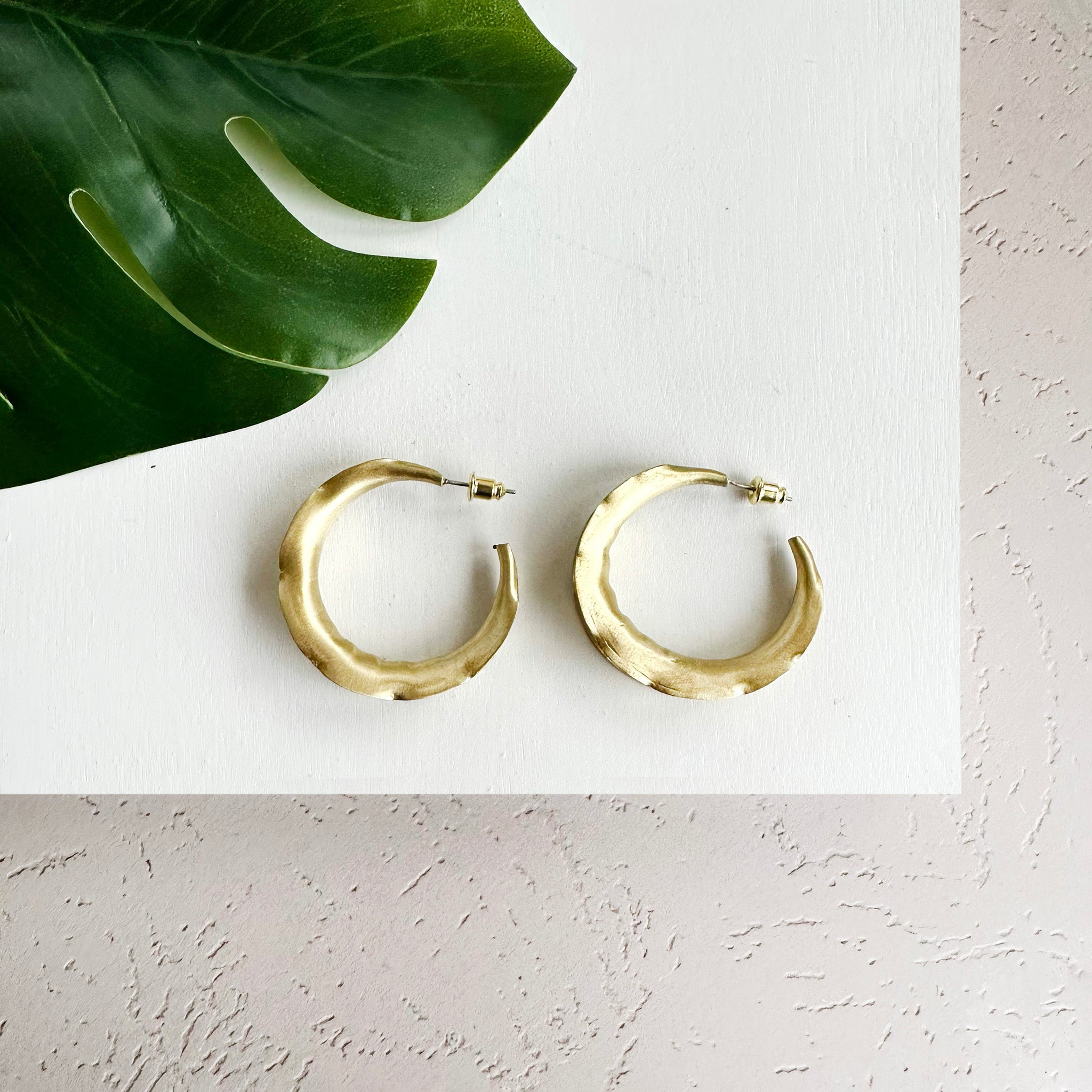 A pair of gold-toned hoops are shown, the edges rippled intentionally for dimension.