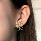 A close-up of a woman's ear is shown, wearing the gold Perennial Posts.