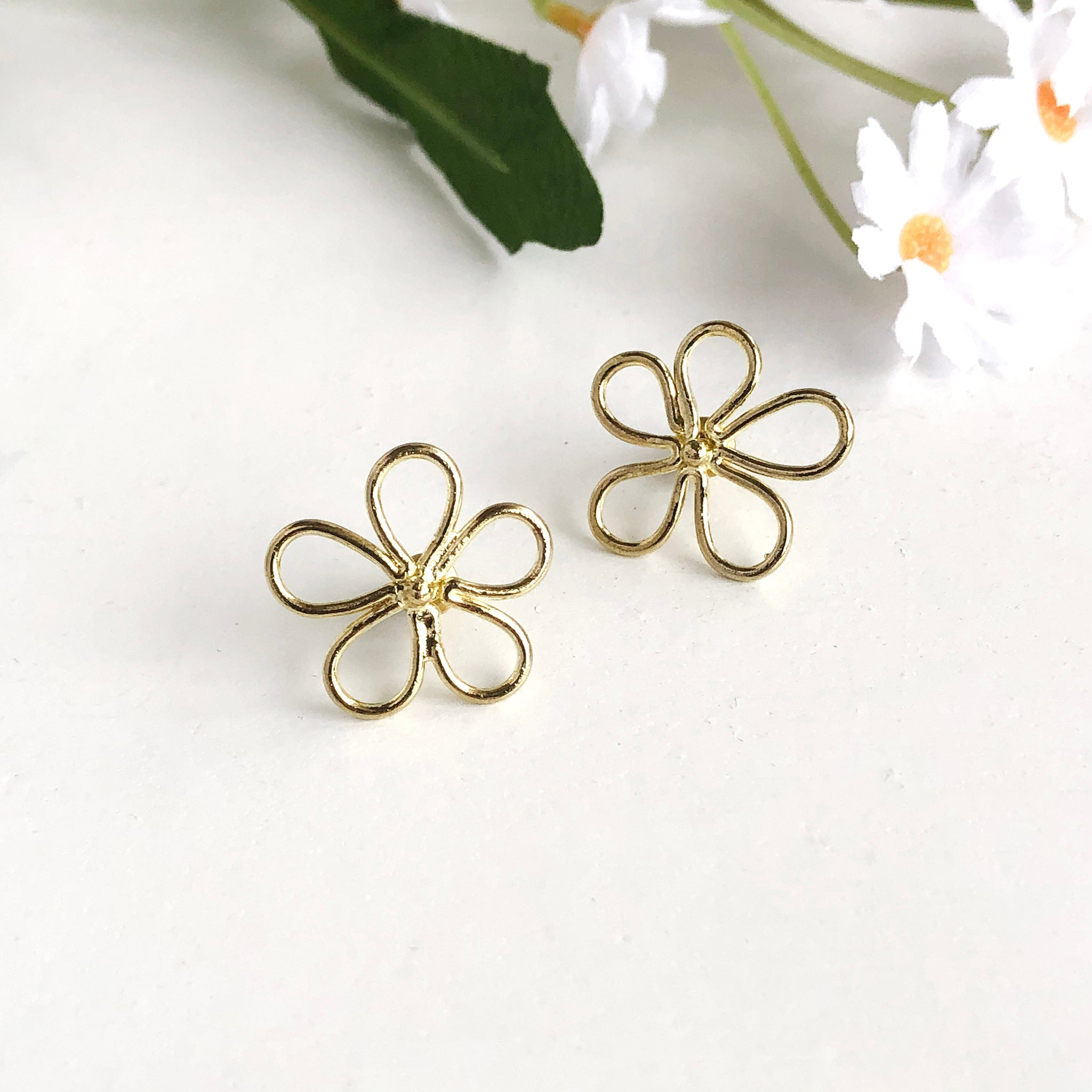 Two earrings are shown. Each is in the shape of a daisy, formed with a single gold wire for an outline-effect.