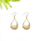 A pair of gold, crescent earrings sits on a white surface with a green leaf in the corner.