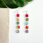 A pair of multicolor beaded earrings is shown against a white background with a green leaf.