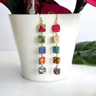 A pair of colorful square-beaded earrings dangles from the edge of a vase.