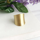 A small, but tall gold ring is placed against green & purple flowers.