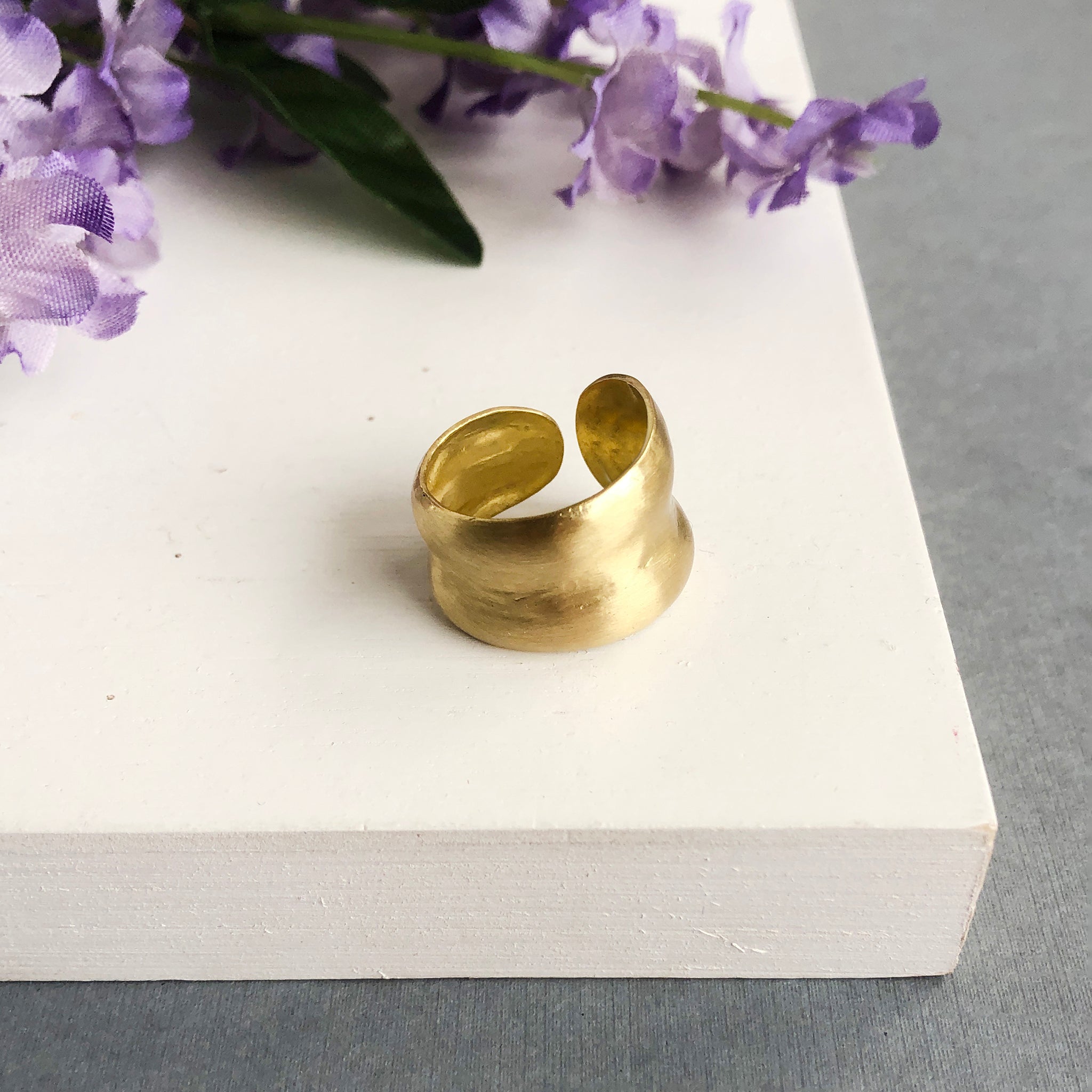 A single gold ring is shown. The sculptural technique gives it a smooth, rounded outer edge with a subtle indent in the center.