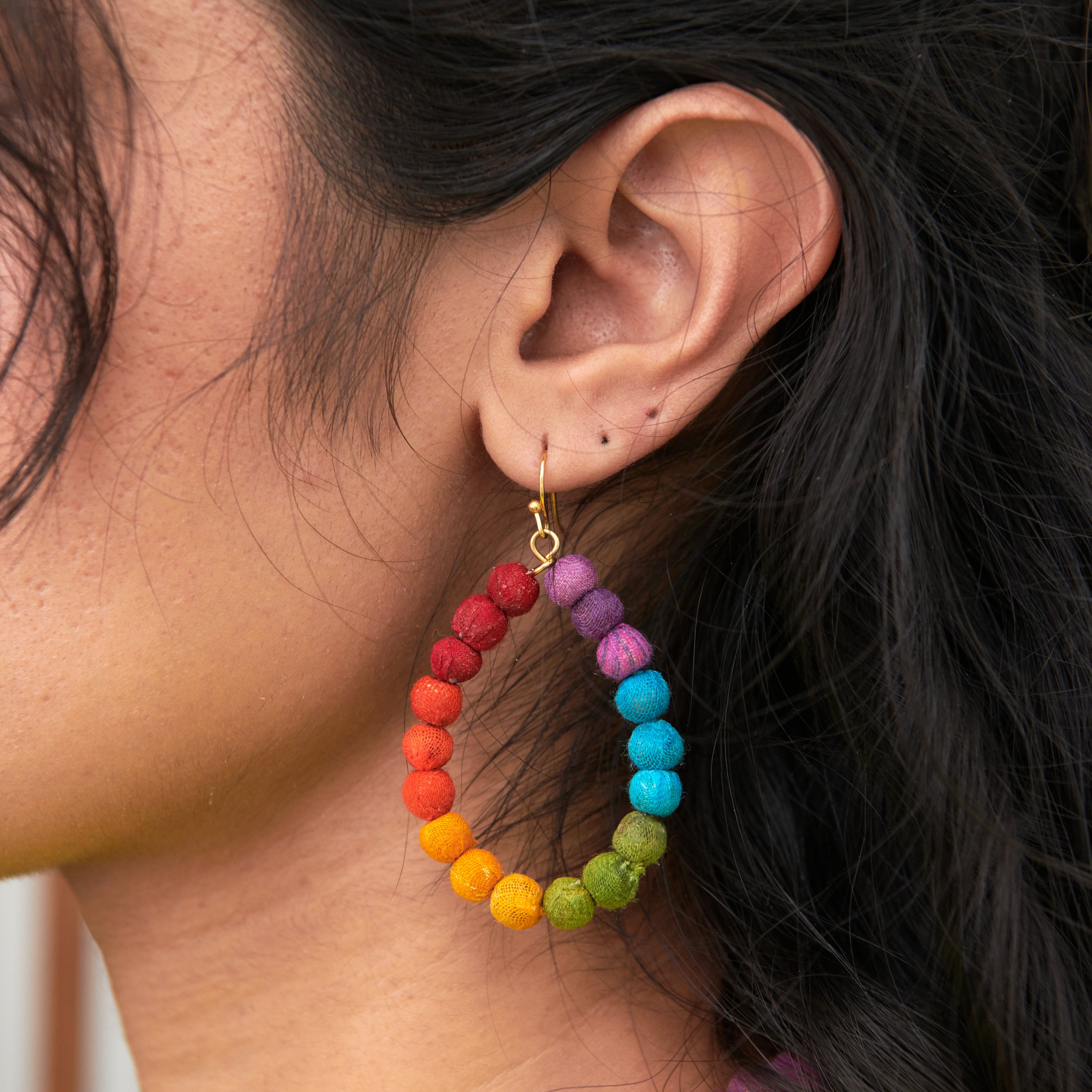 Model wearing Kantha Prism Earrings made of beads that have been sorted and arranged into vibrant, color-blocked sections for an multichromatic rainbow-like display of color.
