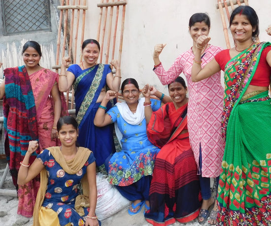 A group of women dressed in Saris hold their arms up and flex their biceps