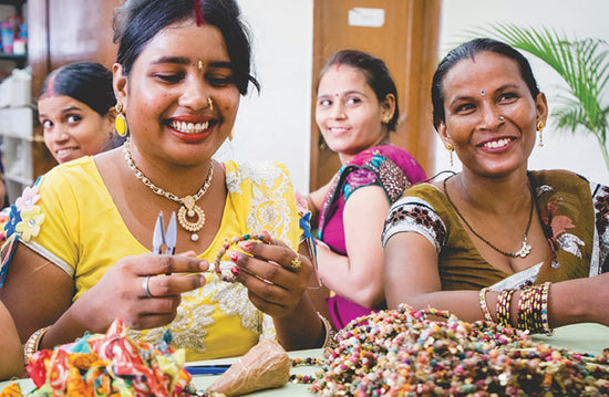 Three women artisans laugh while working amongst completed Kantha bracelets.