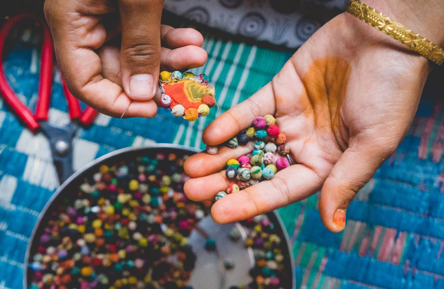 In one hand, an artisan holds an unfinished earring. In the other, a pile of Kantha beads.