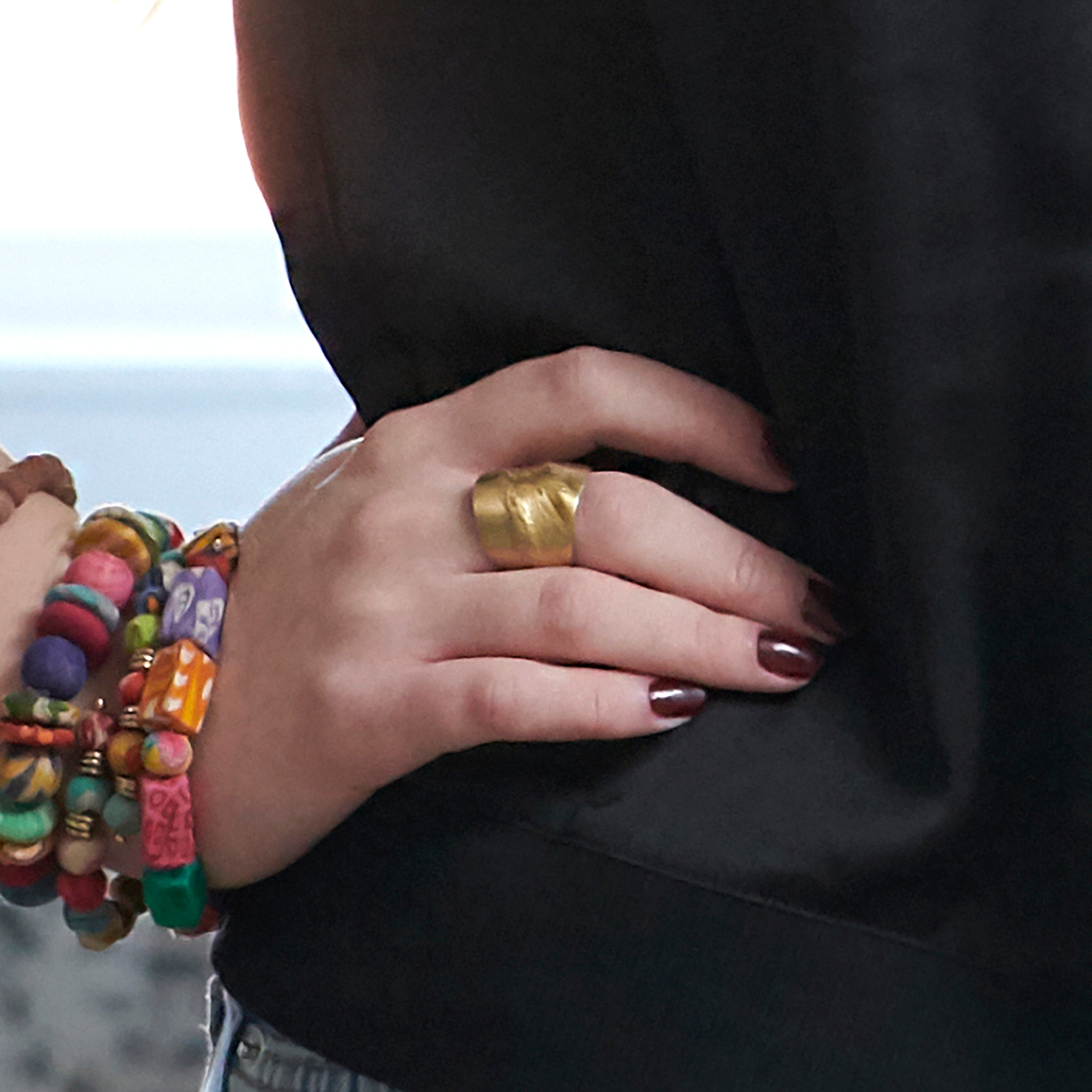 A close up on a woman's hand on her hip featuring a large gold textured ring.