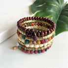 A colorful wrap-style cuff bracelet is shown against a white surface with a dark green leaf in the background.