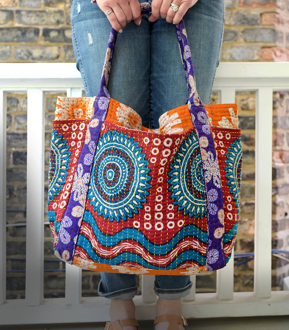A woman holds a vibrant, patterned bag down by her legs.