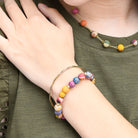 A close up of a woman's wrist resting on her green shirt, and her bracelets she is wearing.