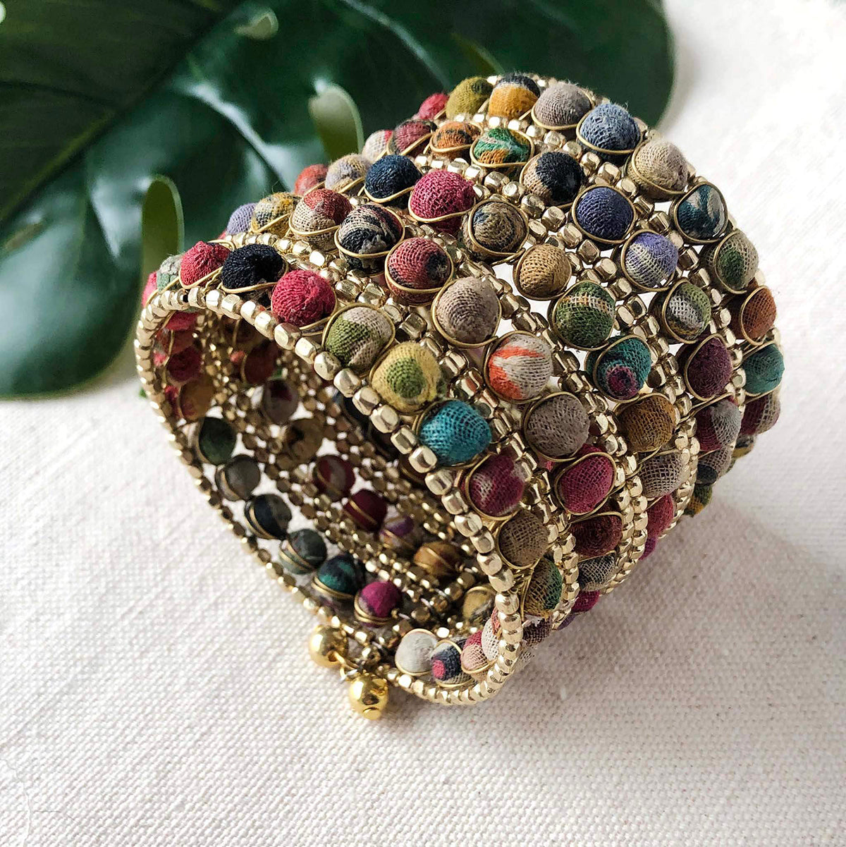 The top of a large cuff bracelet made from colorful textured fabric and gold beads.