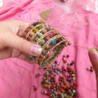 A close up of a woman's hands while she constructs a large beaded cuff bracelet.