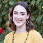 A young woman in a yellow shirt and multicolor beaded jewelry smiles.