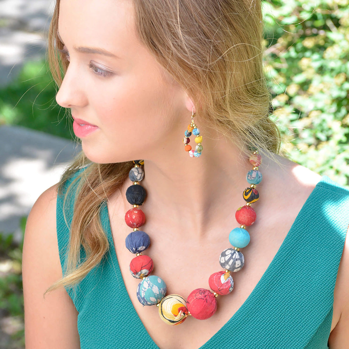 A woman in a teal shirt adorned with multicolor, beaded jewelry.