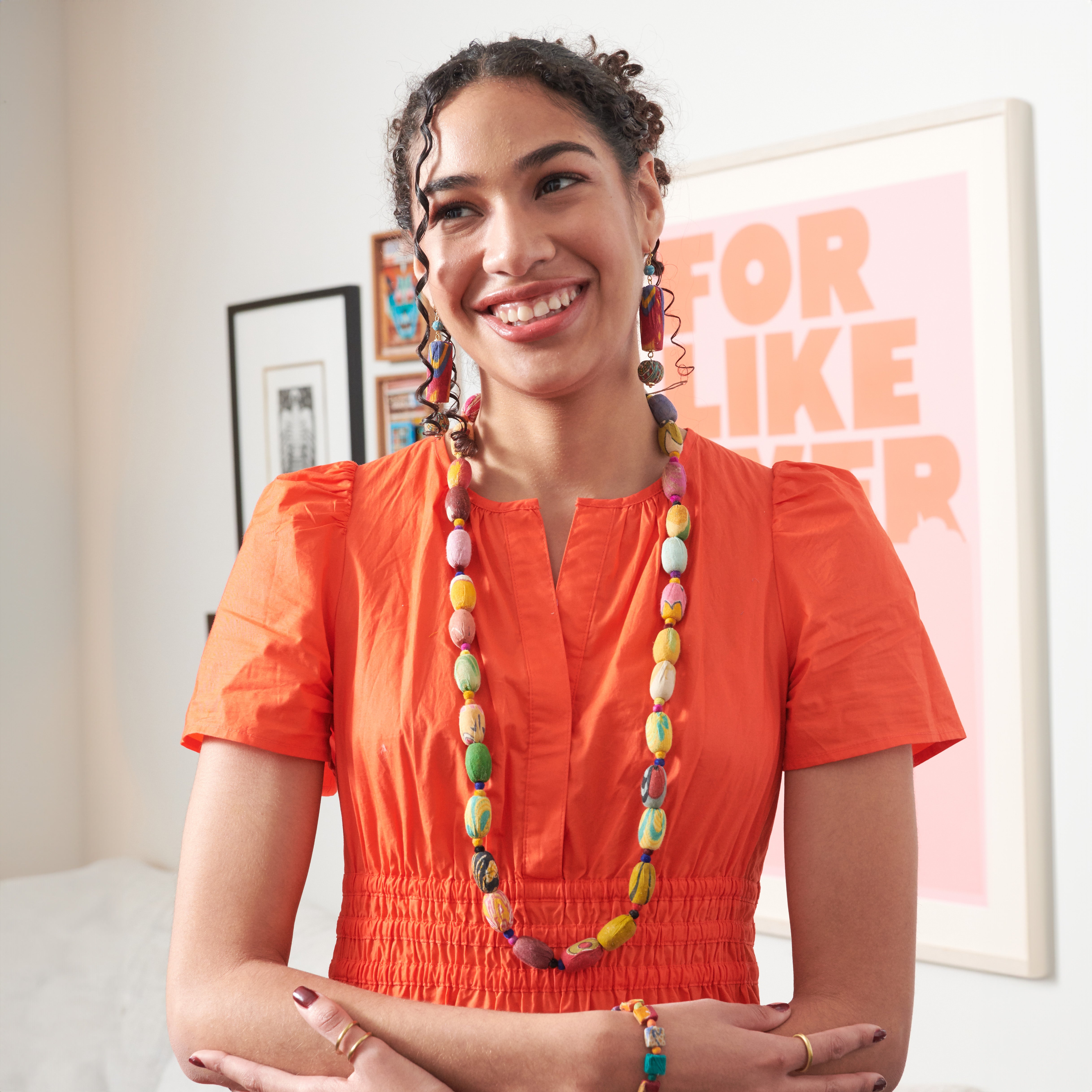 A woman in a yellow top and a multicolor, beaded necklace smiles.