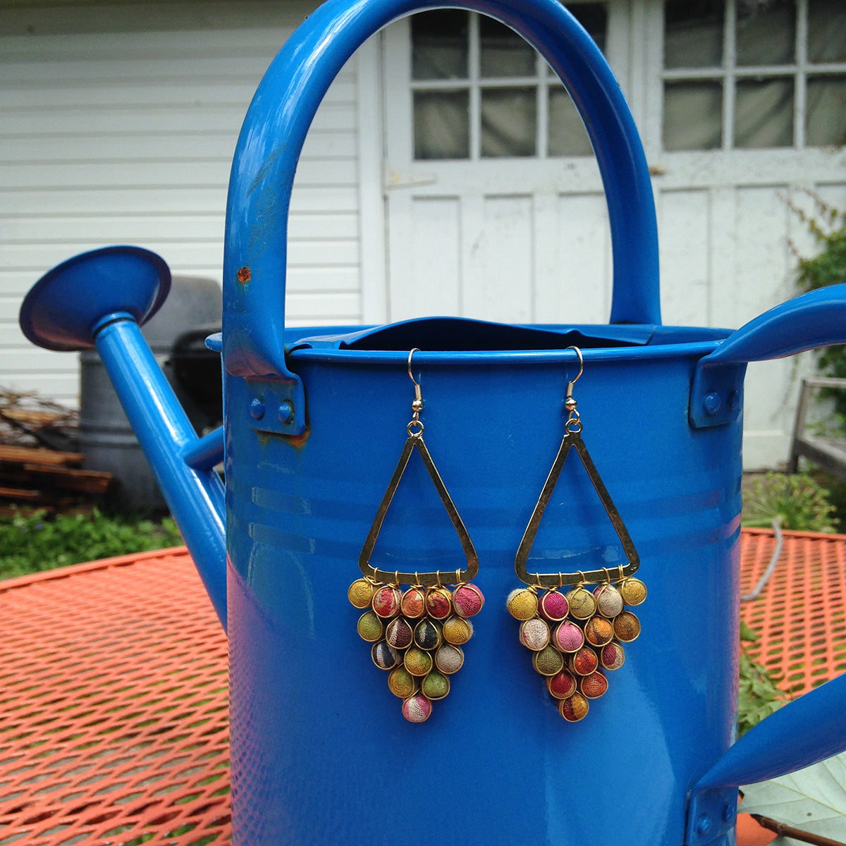 A pair of multicolored beaded earrings dangle from a bright blue watering can.