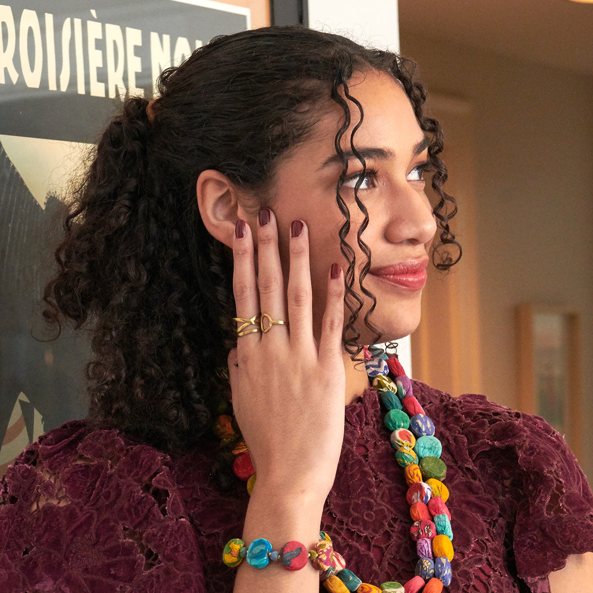 A woman in a red shirt looks off into the distance while resting her hand on her face.
