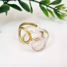 A gold and silver ring are intertwined while resting on a white background with leaves in the background.