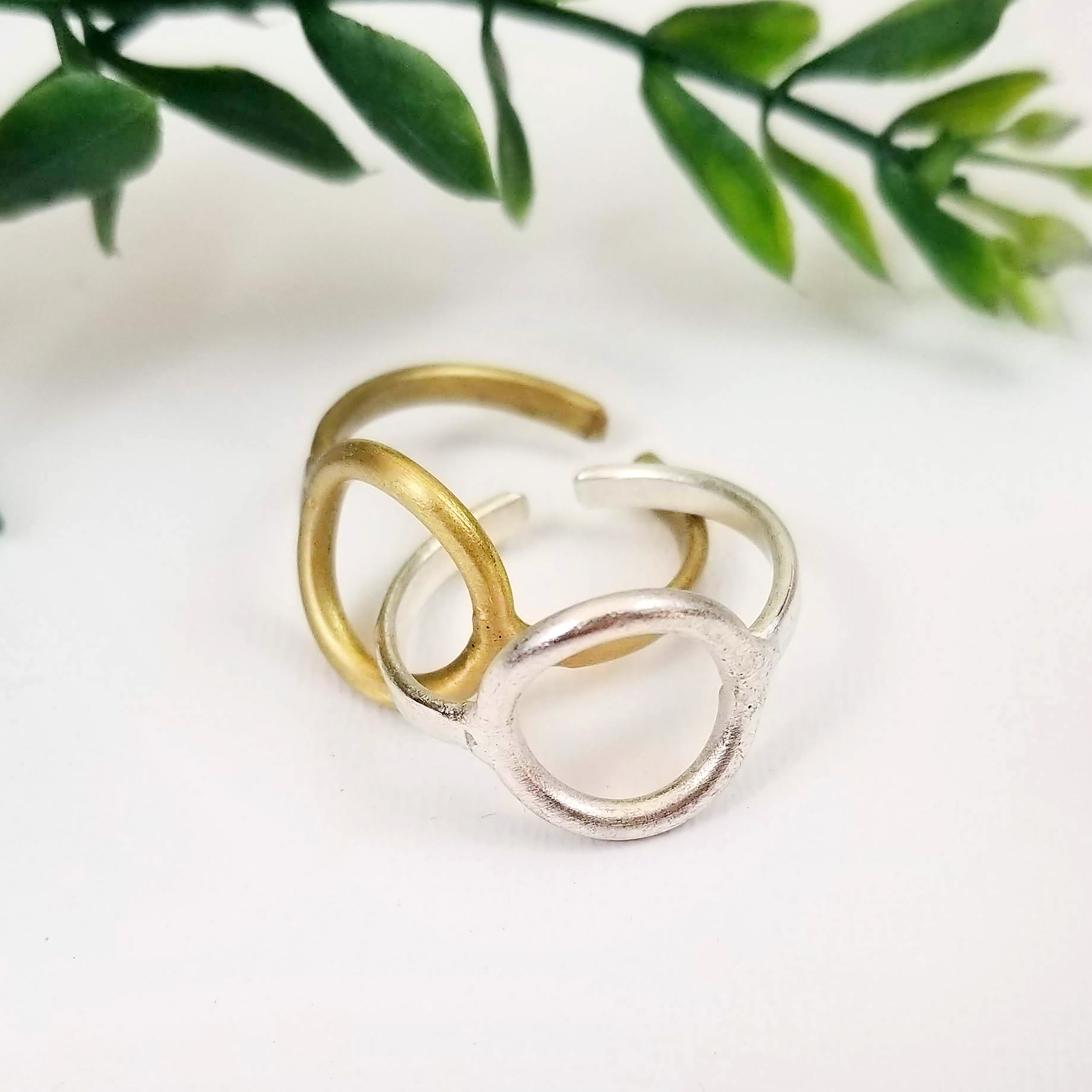 A gold and silver ring are intertwined while resting on a white background with leaves in the background.