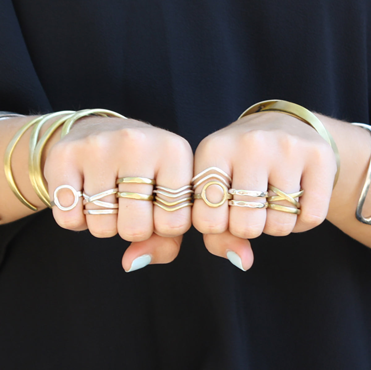 A model shows the fronts of her two fists, each finger adorned with multiple gold and silver rings.