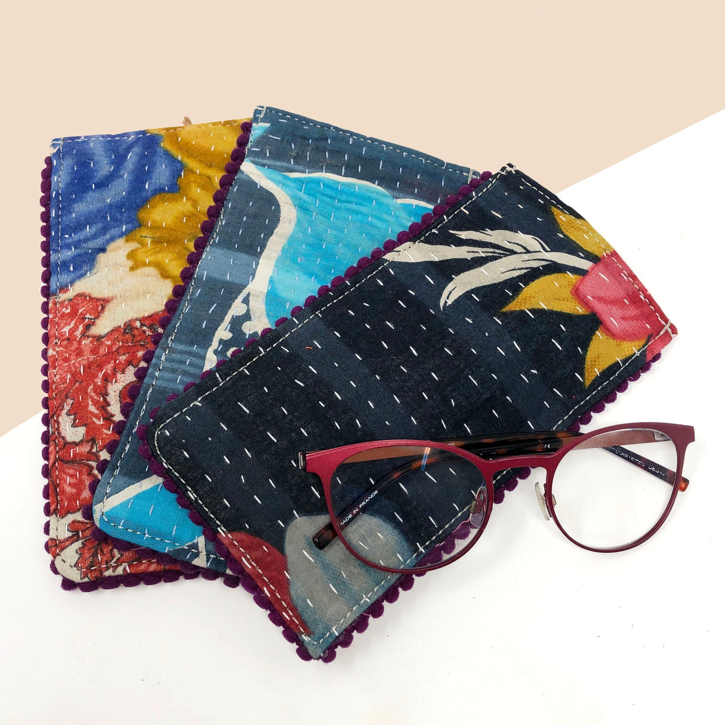 Three soft glasses cases are fanned out with a pair of glasses placed atop them.