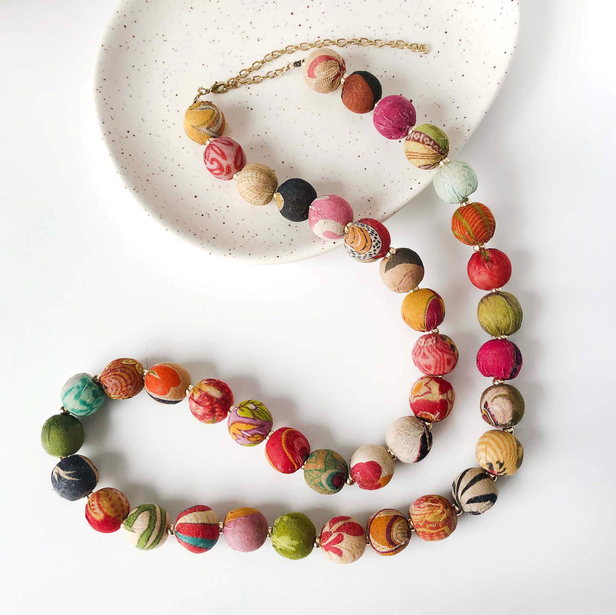 A single strand of colorful textile-covered beads winds on a table to create a necklace.