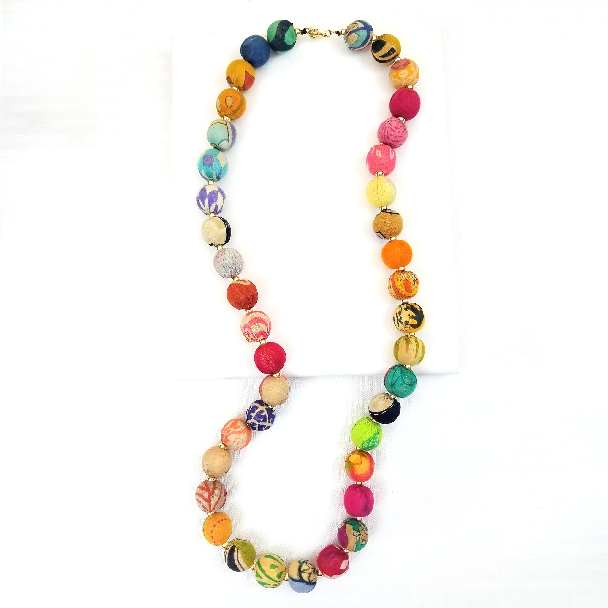 A single colorful Kantha Garland Necklace rests on a white table.