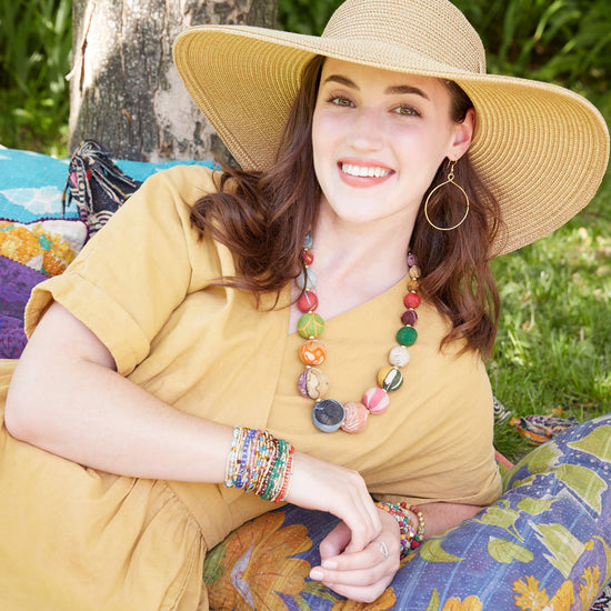 A model in yellow wears the Kantha Graduated Bead Statement Necklace and a stack of delicate beaded bracelets.