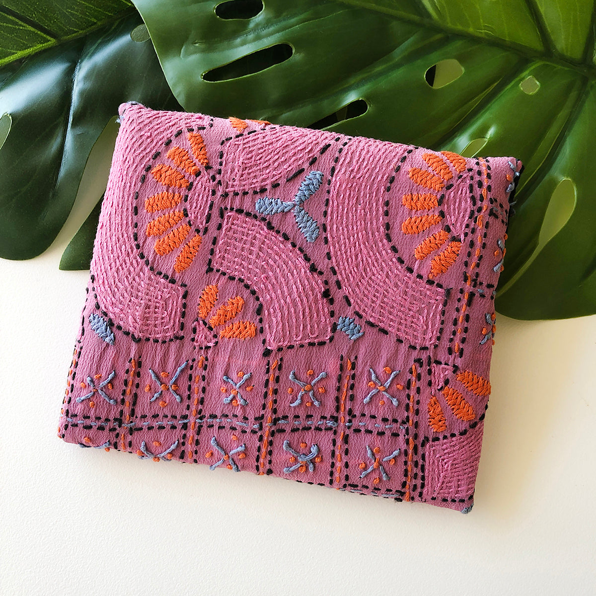 A pink envelope-style pouch features traditional embroidery techniques.