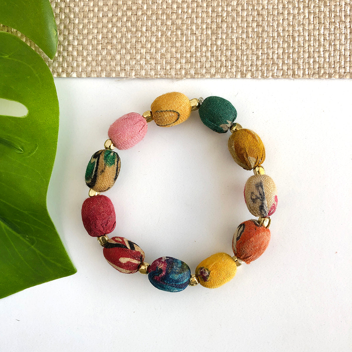 A colorful strand of textile-wrapped oblong beads is spaced out with small gold beads to create a bracelet.