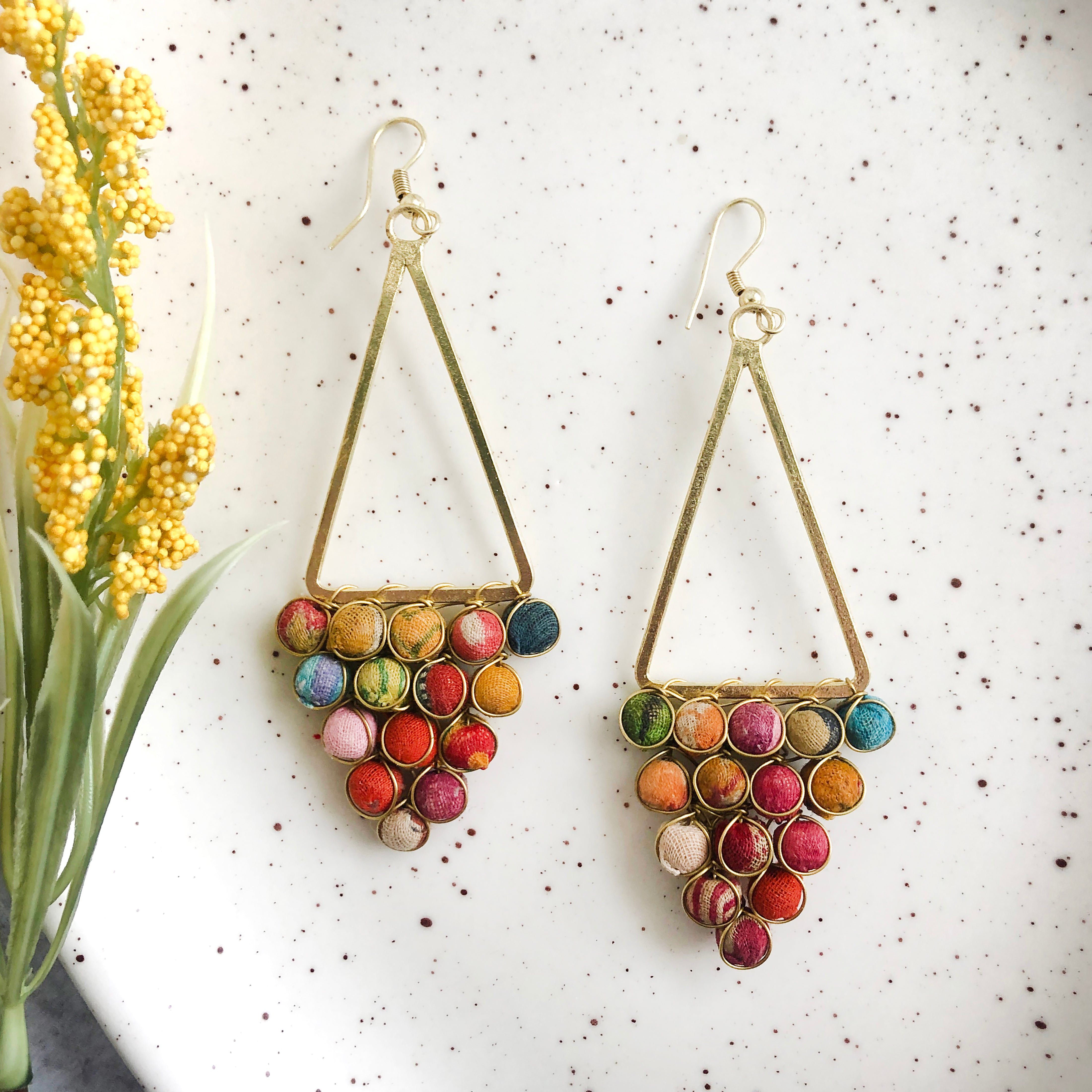 A triangle made from textile-wrapped beads and gold wire hangs from a golden triangle frame to form these earrings.
