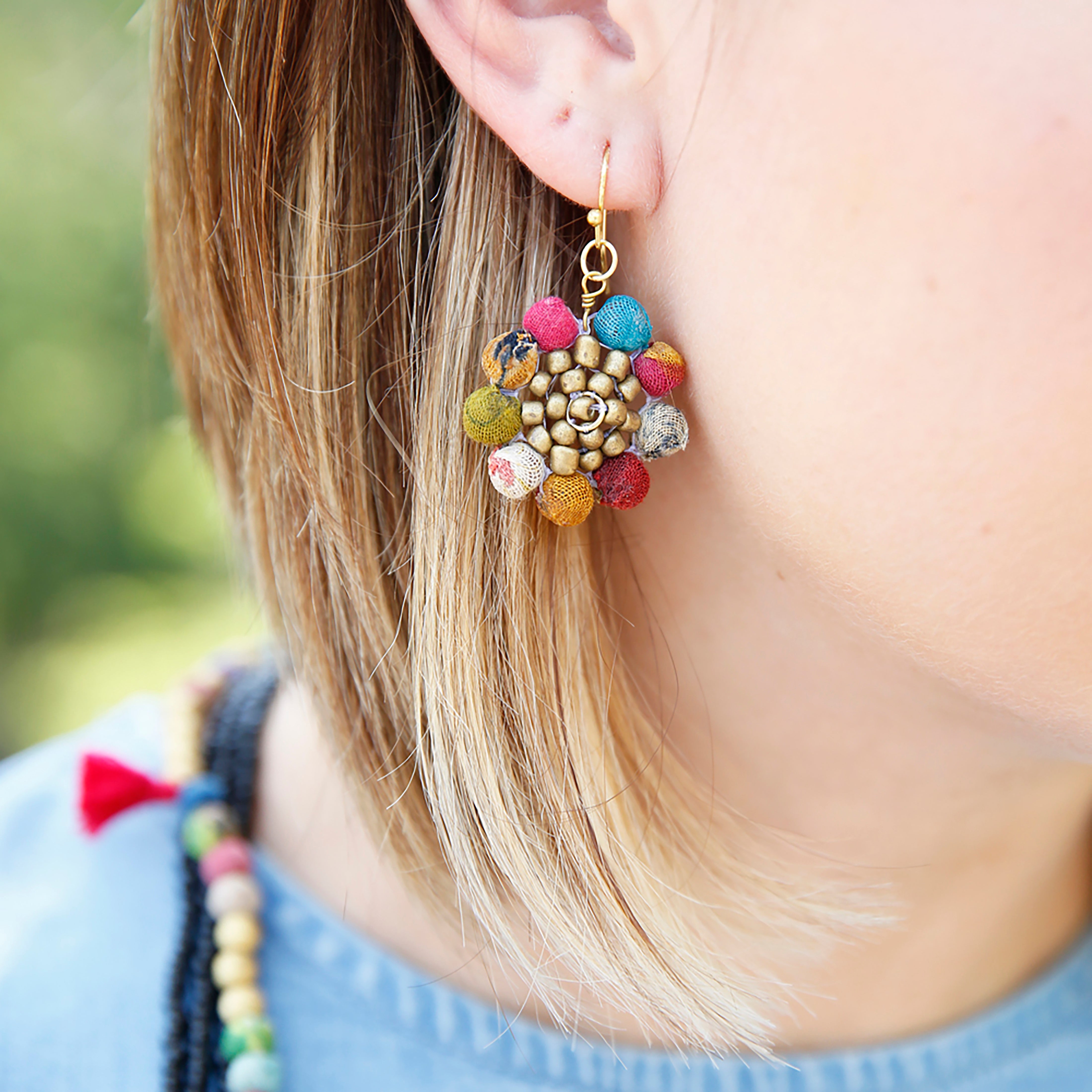 A pair of Kantha Sunflower Earrings adorns a woman's ear.