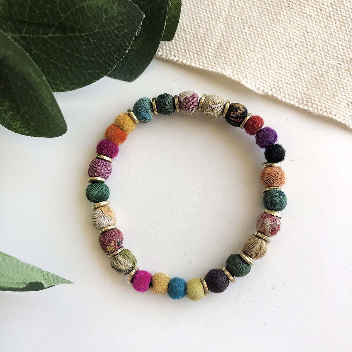 Load image into Gallery viewer, A multicolored bracelet sits amongst some greenery
