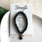 A black beaded bracelet is attached to a card that reads "Strength"