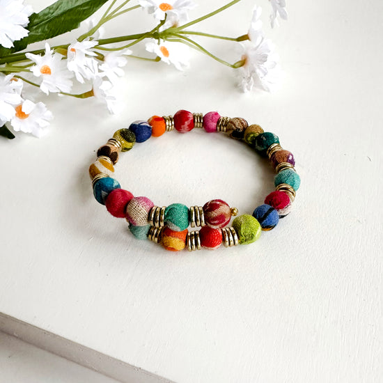 Colorful round textile-wrapped beads and a trio of brass discs spiral around to create a bangle-style bracelet.