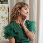 A woman touches her face and looks into the distance, showing off the bracelets on her wrist.